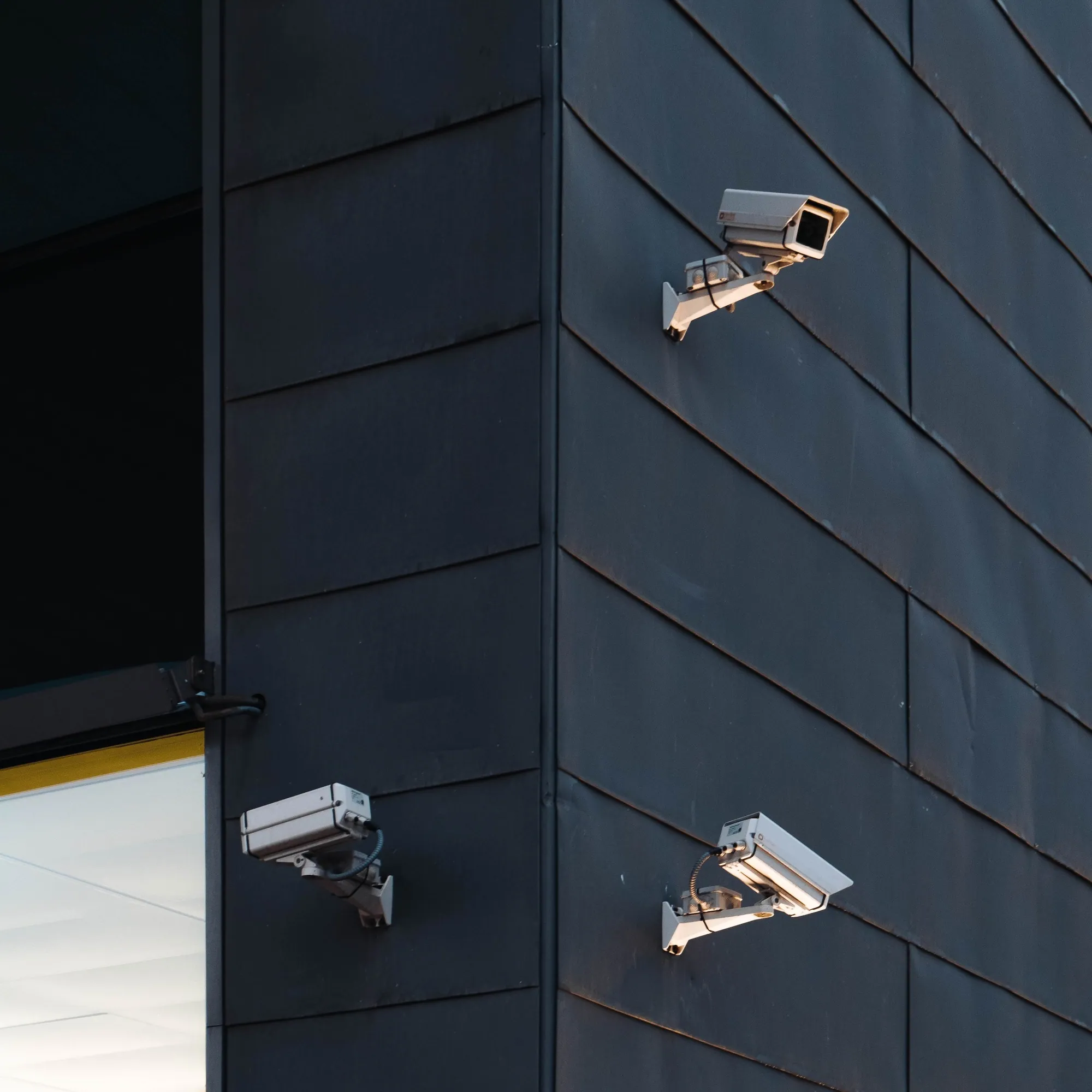 Three CCTV cameras on the corner of a dark building