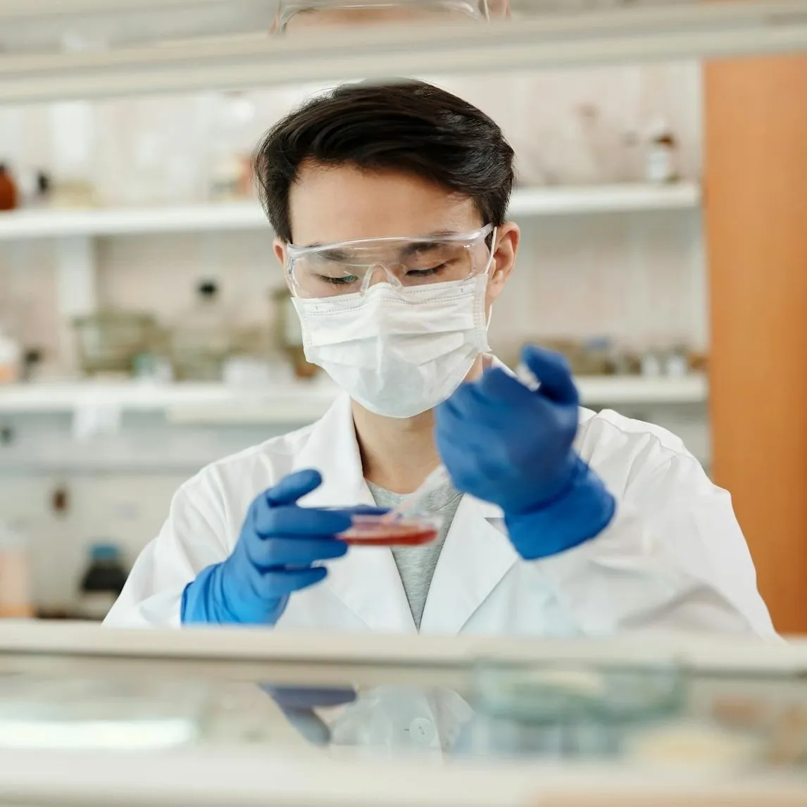 Scientist in a face mask examining a sample in a laboratory